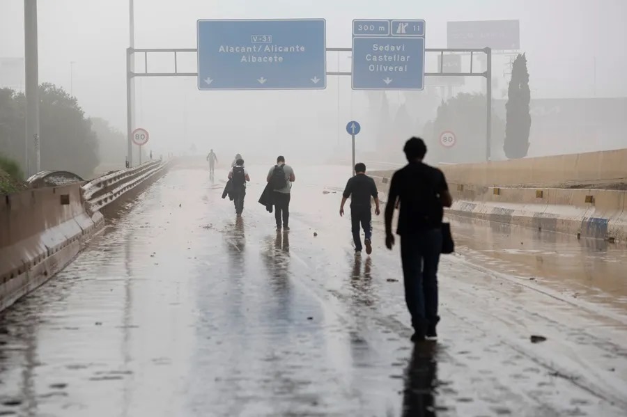 Varias personas transitan por la V-31 cerrada al tráfico a causa de las lluvias torrenciales de las últimas horas. EFE/Miguel Ángel Polo